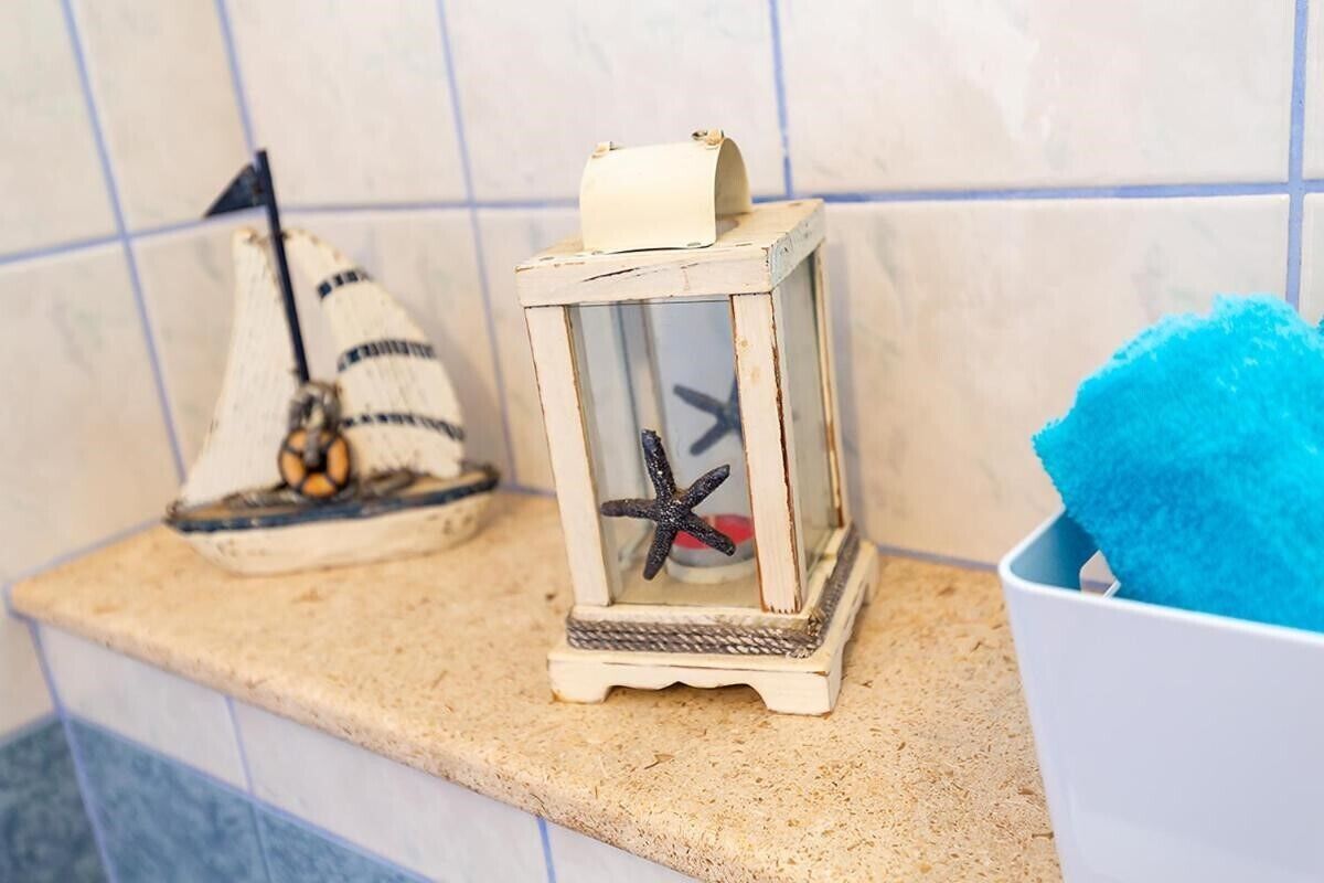 Eine Küchenarbeitsplatte mit einem weißen Keramikbecken, einem kleinen weißen Schrank und einem blauen Schwamm.