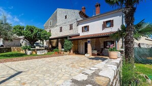 Una casa de dos pisos con un patio de piedra, un pequeño jardín y una palmera.