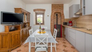 Una cocina compacta con televisión, armarios de madera, horno de ladrillo y comedor con mesa y sillas.