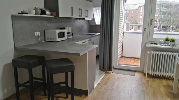 Una cocina moderna con una isla central, taburetes de bar, microondas y ventana con vista a una zona residencial.