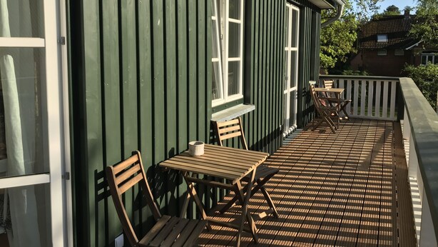 En træterrasse med et bord, stole, et vindue og et gelænder.
