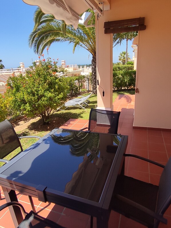 Une terrasse avec une table et des chaises en verre, un parasol blanc et une vue sur des palmiers et des immeubles.