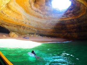Une personne nage dans une piscine, avec une formation rocheuse en forme de grotte en arrière-plan.
