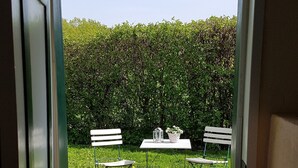A doorway leading to an outdoor patio with two white benches and a table with a potted plant. - Summer in the old stable (Iserlohn)
