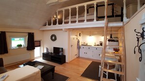 A cozy, well-lit room with a TV, a dining table, and a kitchen area with a sink and cabinets. - Summer in the old stable (Iserlohn)