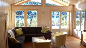 A wooden interior with a sectional sofa, armchairs, and a wooden table. Large windows provide views of a snowy landscape. - panorama view, modern apartment, quiet location, canoe, sauna (Amli/Felle)