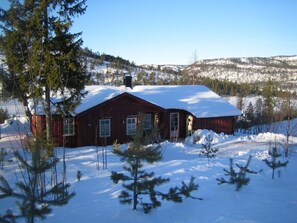 Eine rote Holzhütte mit einem schneebedeckten Dach, umgeben von Schnee und Bäumen.