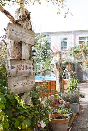 A wooden signpost with directional arrows pointing to 'URLAUBSLOFT,' 'SAUNA,' and 'FITNESSRAUMA.'