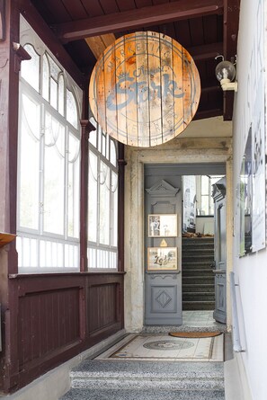 A wooden door with a circular sign above it, a staircase leading to an upper level, and a wall with framed pictures.