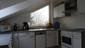 Een moderne keuken met witte kasten, een magnetron, een koffiezetapparaat en een groot raam.