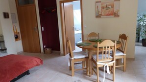 Een kamer met een bed, een eettafel met stoelen, een rode deur en een schilderij aan de muur.