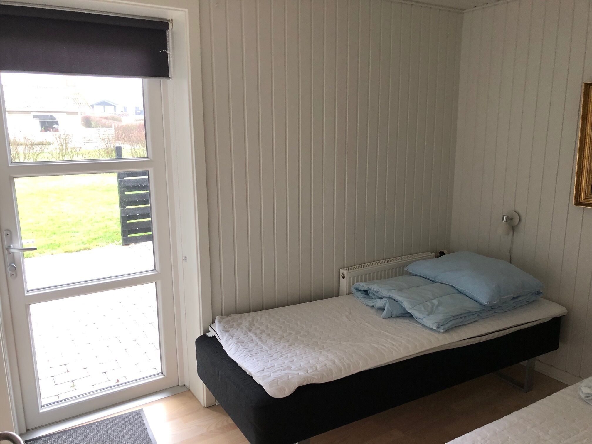 Quarto pequeno com uma cama de solteiro, janela e radiador.