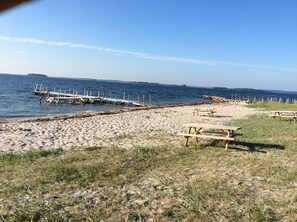 A beach with wooden picnic tables and a pier extending into the water.