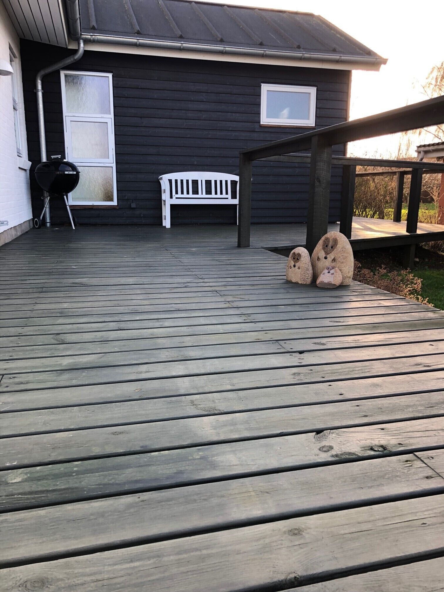A wooden deck with a grill, a white bench, and two decorative animal figures.