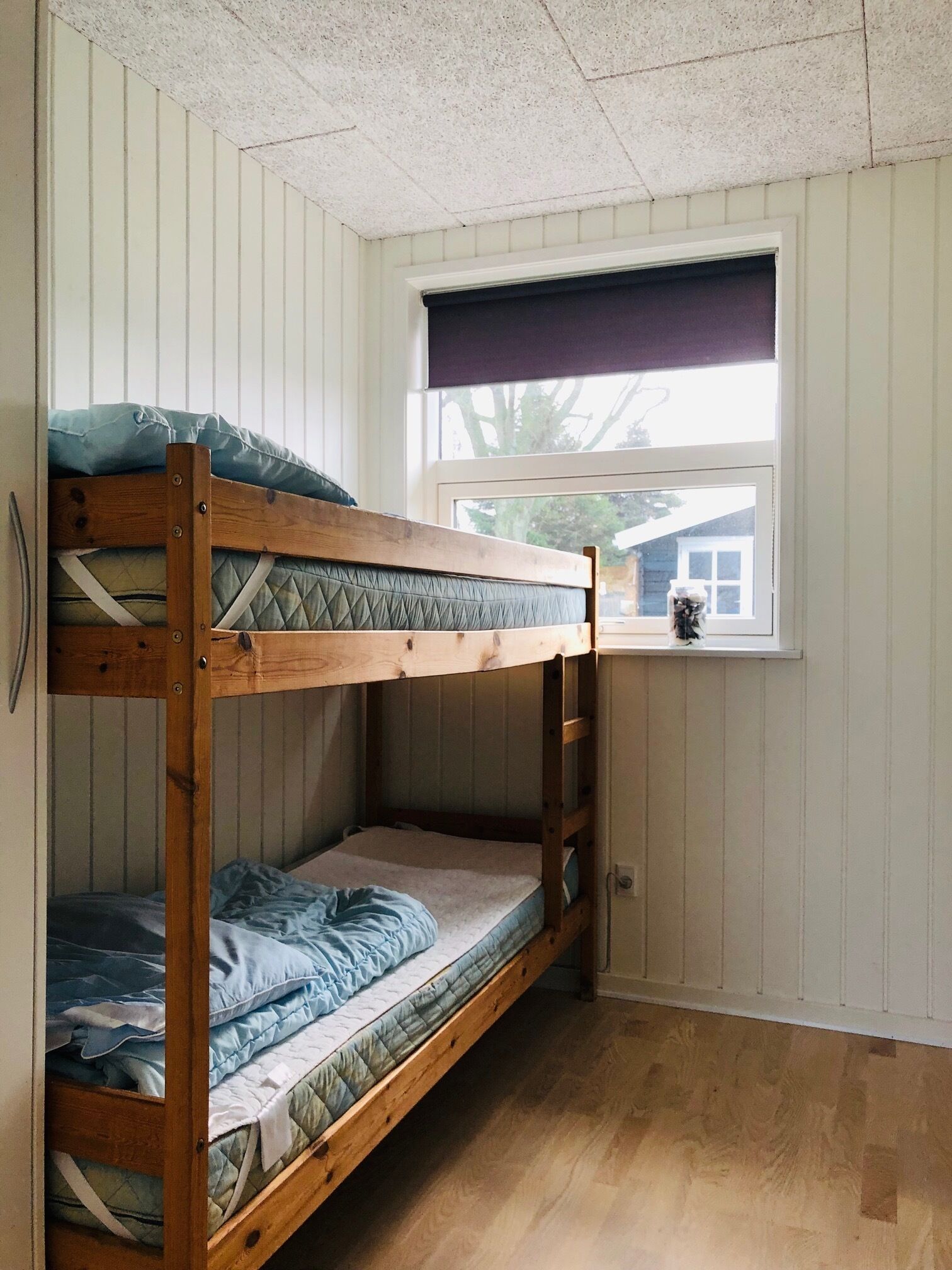 Een stapelbed in een kamer met houten wanden en een raam met uitzicht op een huis.