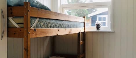 Een stapelbed in een kamer met houten wanden en een raam met uitzicht op een huis.