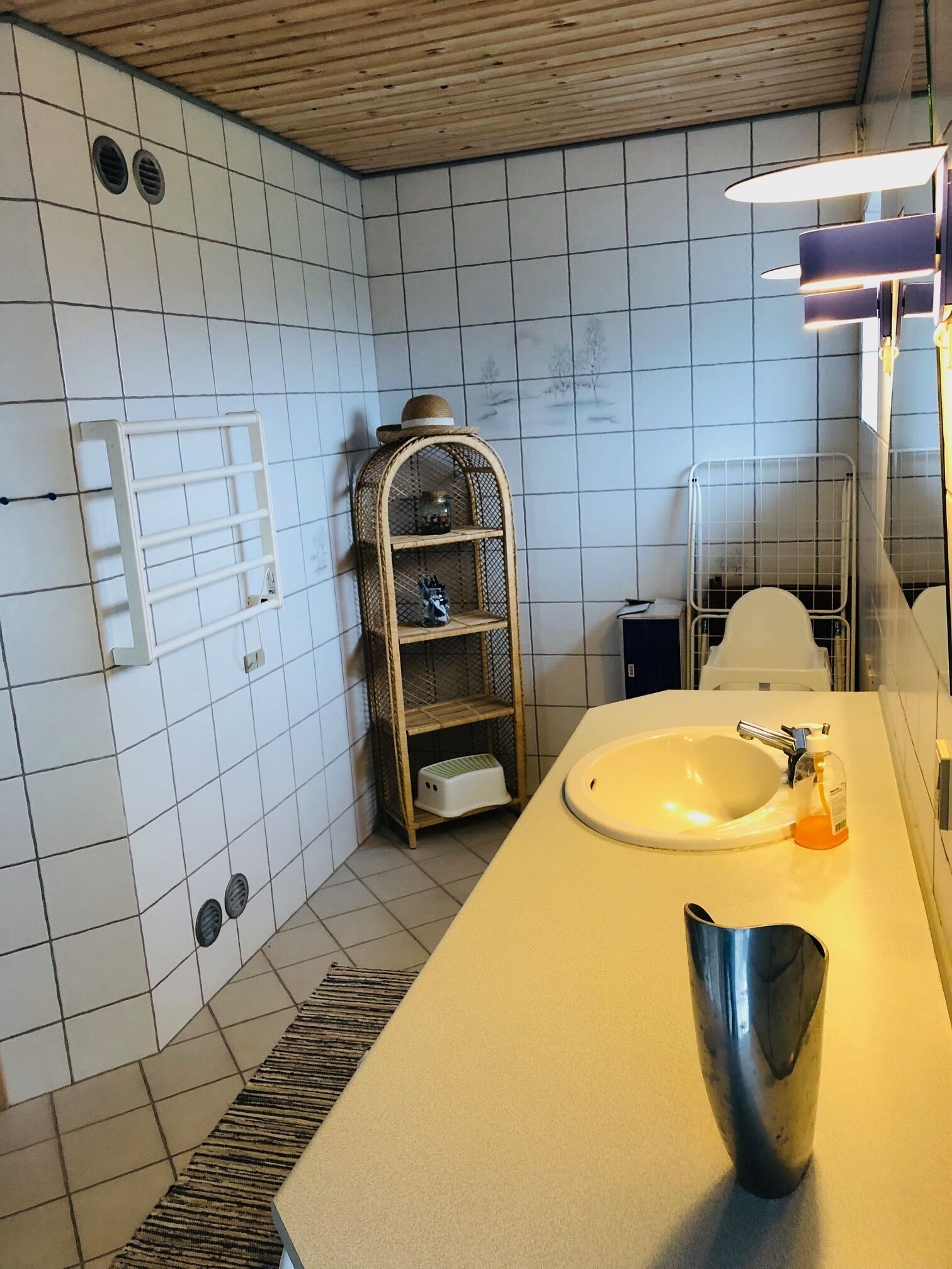 A bathroom with a white sink, a mirror, and a shelf with toiletries.