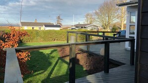 Eine Holzterrasse mit Metallgeländer, eine Rasenfläche mit Büschen und im Hintergrund eine Ansicht von Häusern und Bäumen.