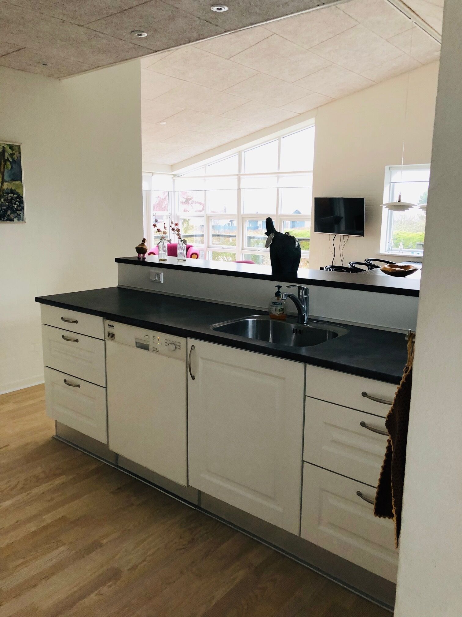 A kitchen with a black countertop, white cabinets, a stainless steel sink, and a window with a view of greenery.