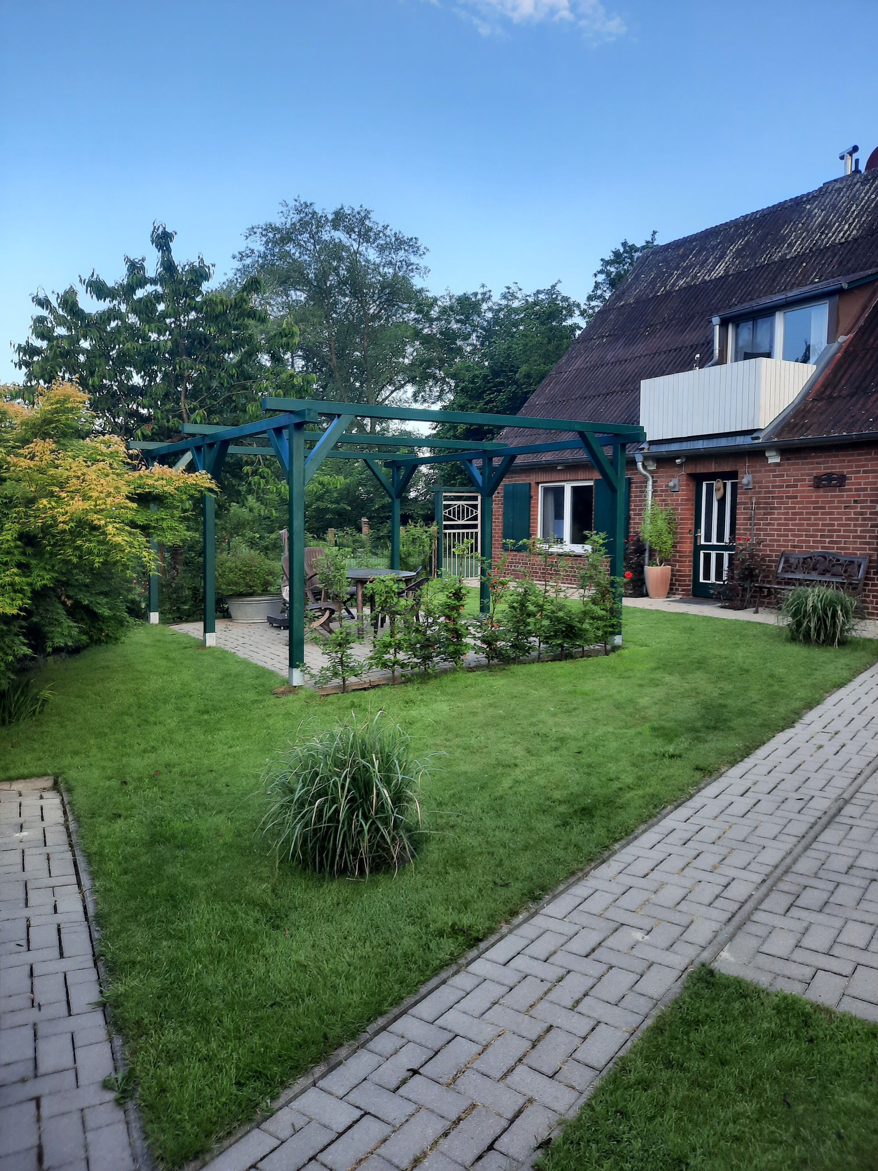 Ein Garten mit einem grünen Pergola, einem Ziegelhaus und einem gepflasterten Weg.
