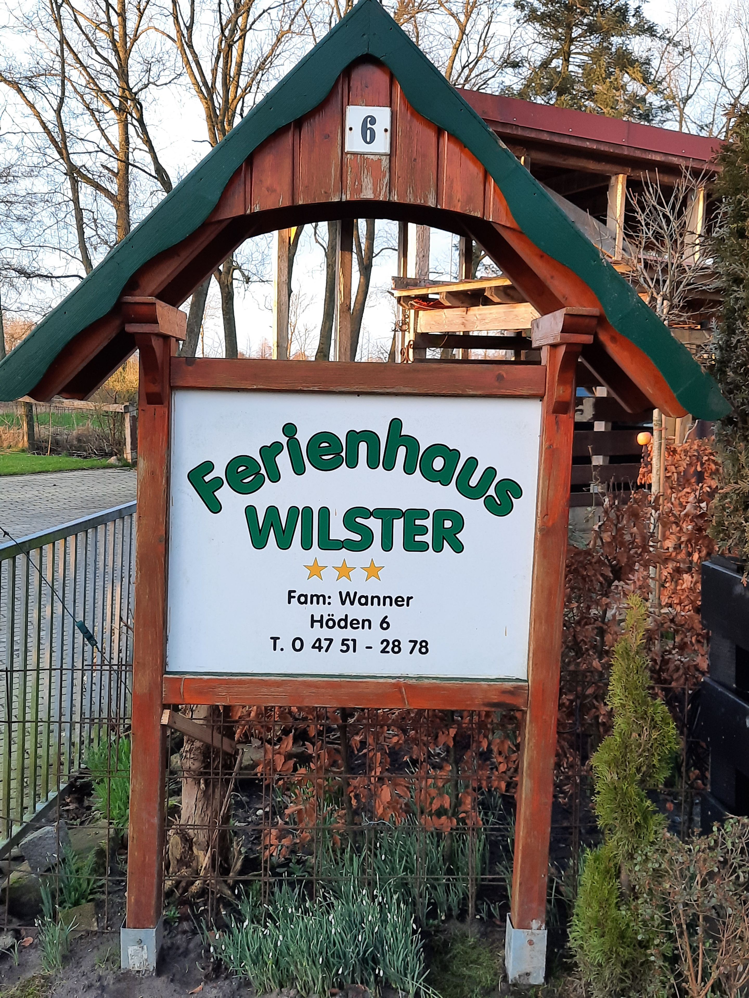 Une pancarte en bois portant l’inscription « Ferienhaus Wilster » et les coordonnées.