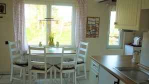 A dining area with a round table, white chairs, a vase with flowers, and a bulletin board on the wall. - 3-star ground floor, free Wi-Fi, near the coast in Otterndorf (Neuenkirchen)