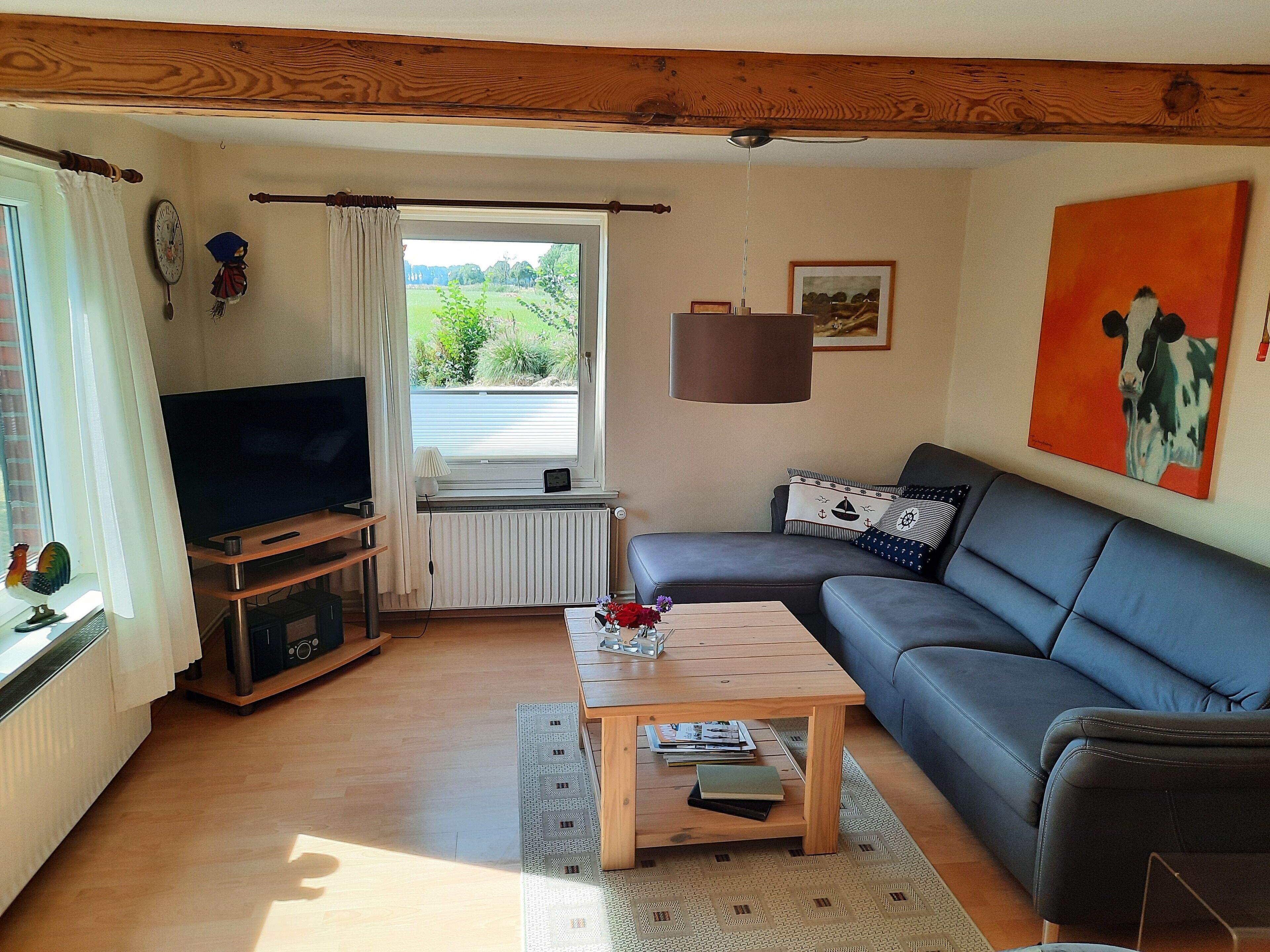 Ein Wohnzimmer mit Fernseher, einer Couch, einem Couchtisch und einem Fenster mit Vorhängen.