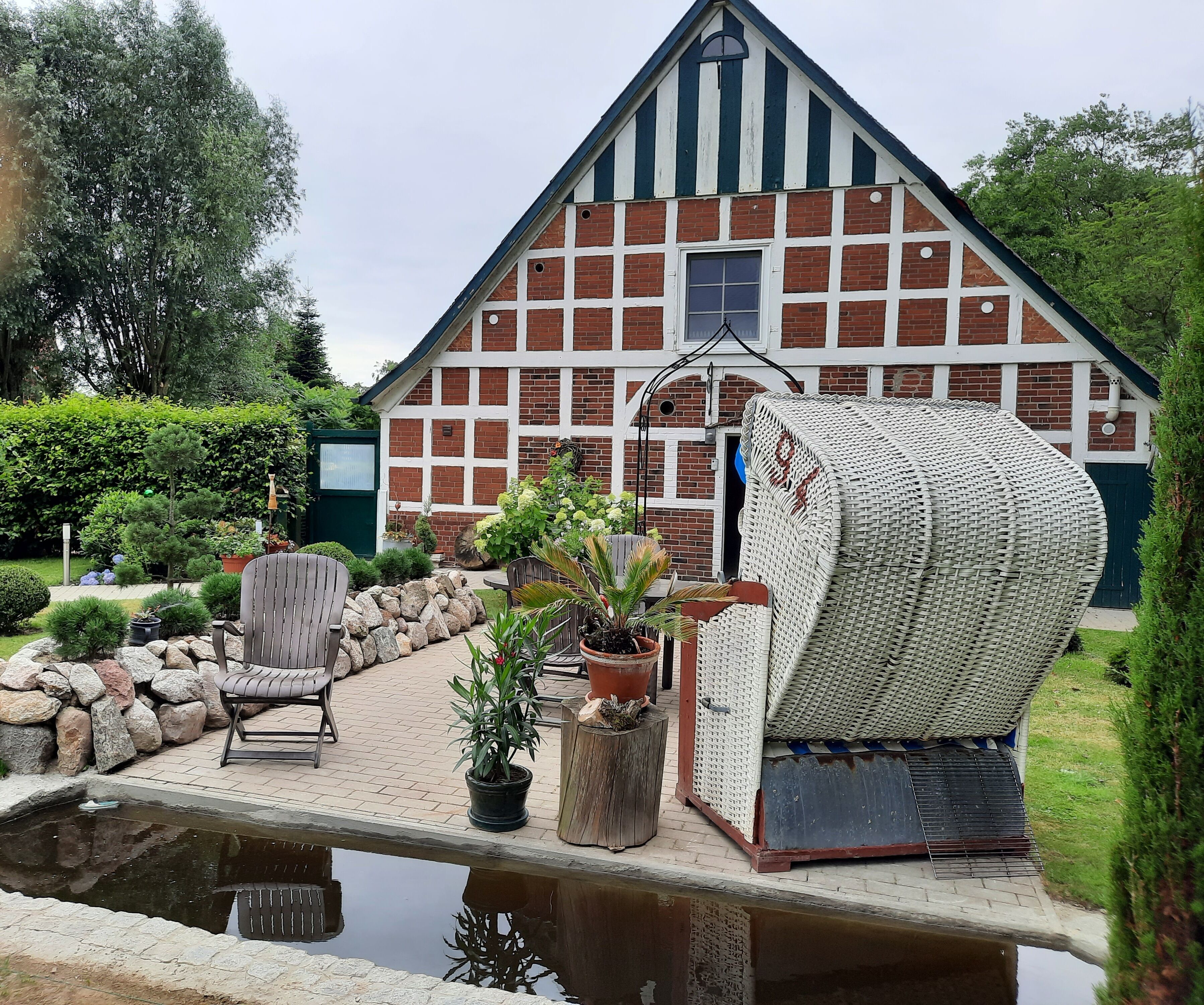 A traditional half-timbered house with a pond, outdoor seating, and potted plants.