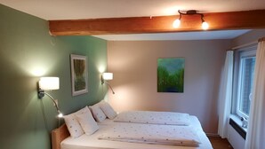 A bedroom with a wooden bed, two wall-mounted lamps, a painting, and a window with curtains. - 3-star ground floor, free Wi-Fi, near the coast in Otterndorf (Neuenkirchen)