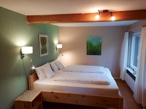 Ein Schlafzimmer mit einem hölzernen Bett, zwei Wandlampen, einem Gemälde und einem Fenster mit Vorhängen.
