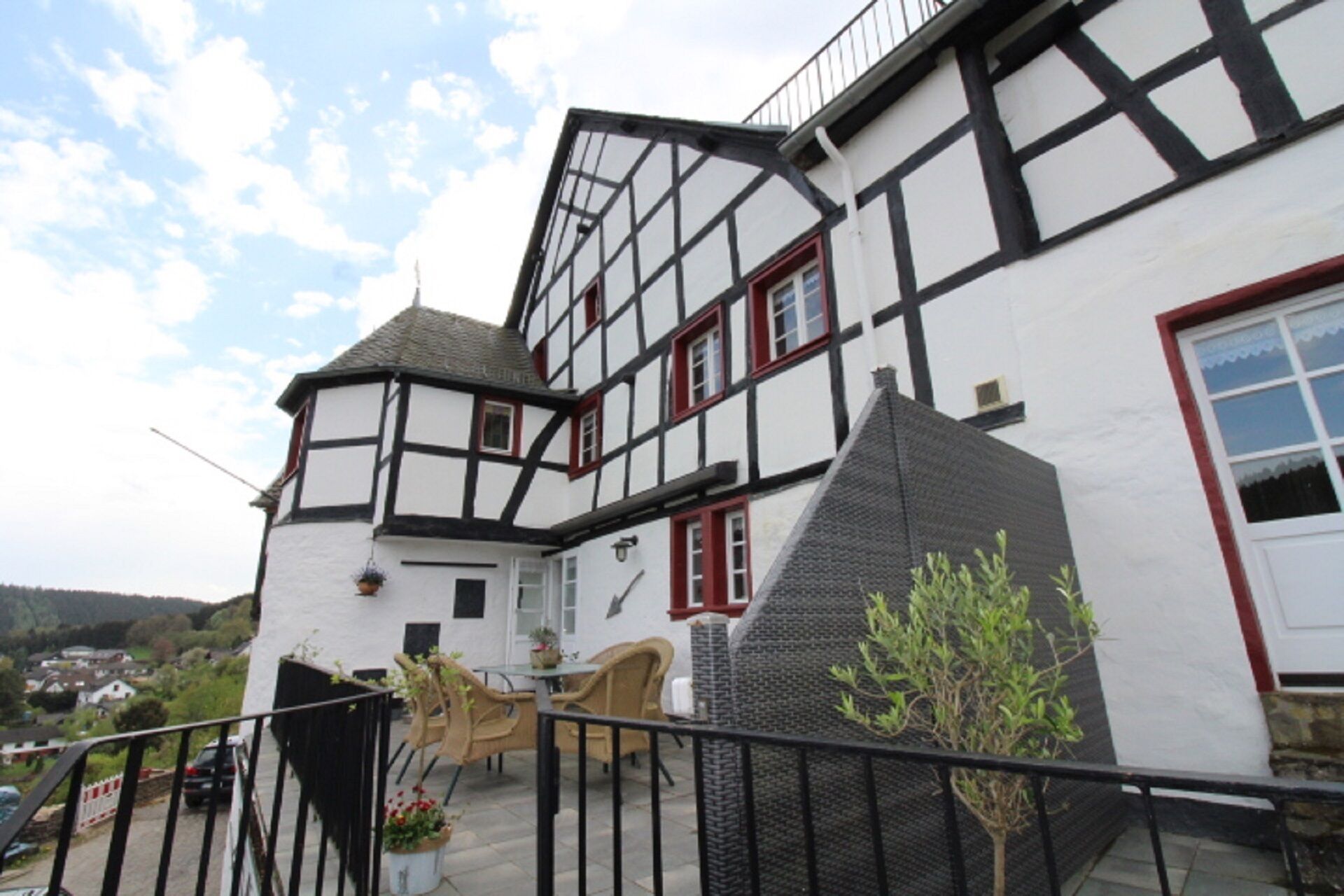 Een tweetalig Tudor-stijl gebouw met balkon, een kleine tuin en uitzicht op de omgeving.