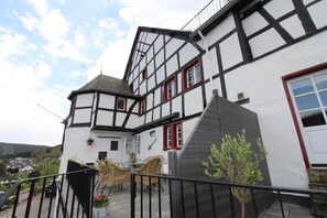 A two-story Tudor-style building with a balcony, a small garden, and a view of the surrounding area.