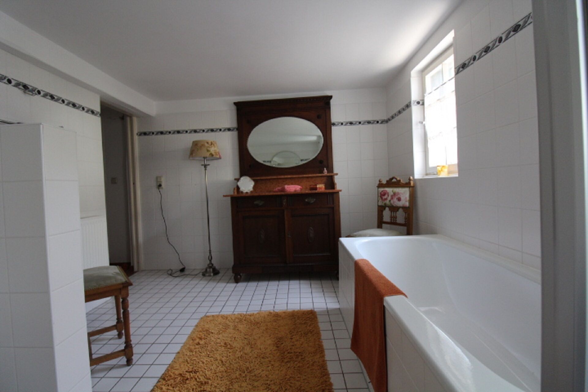 Un bagno con una vasca da bagno bianca, un mobile bagno in legno con uno specchio, un tavolino e una lampada da terra.