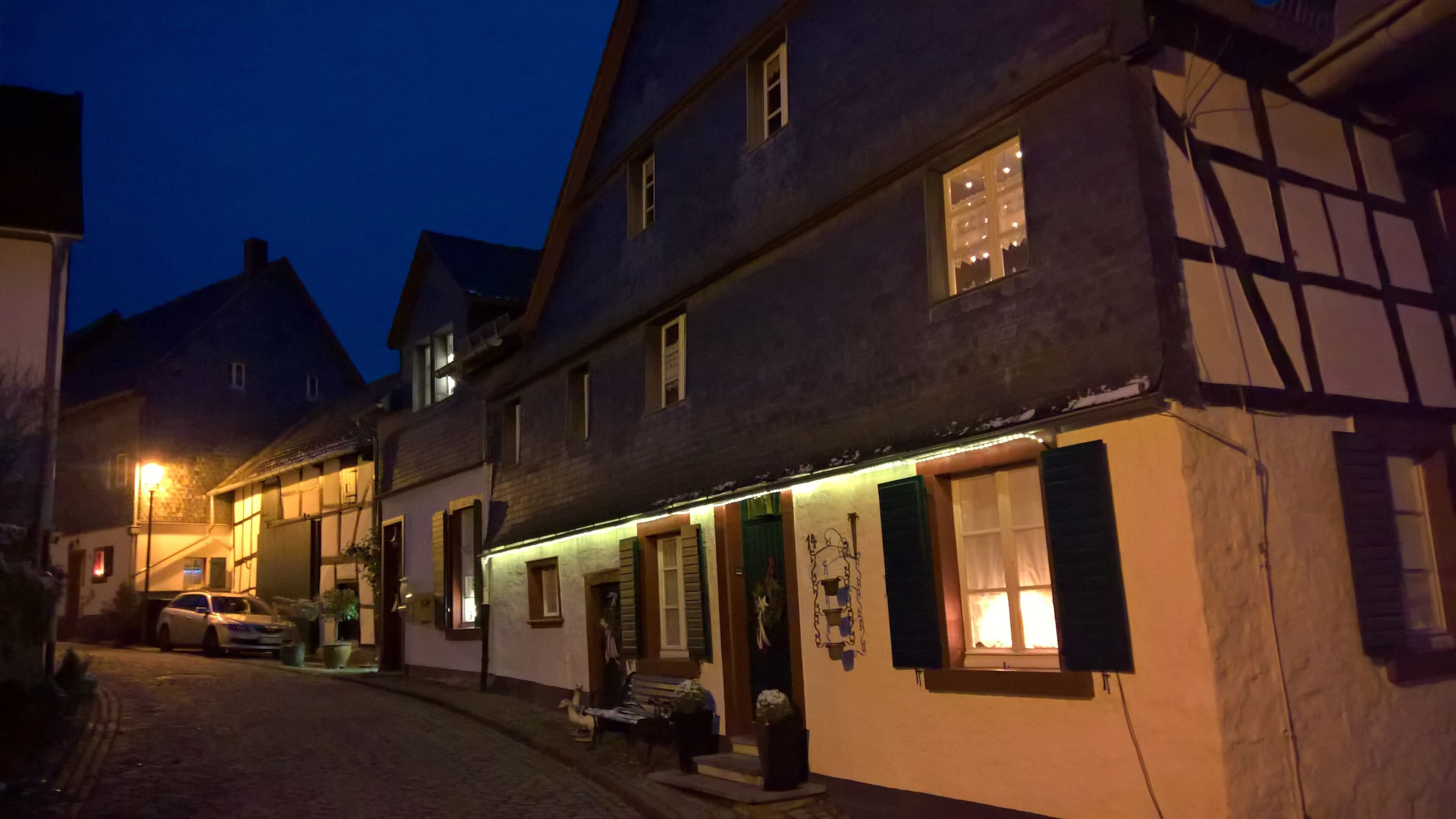 A traditional European building with a cobblestone street, a bench outside, and a car parked nearby.