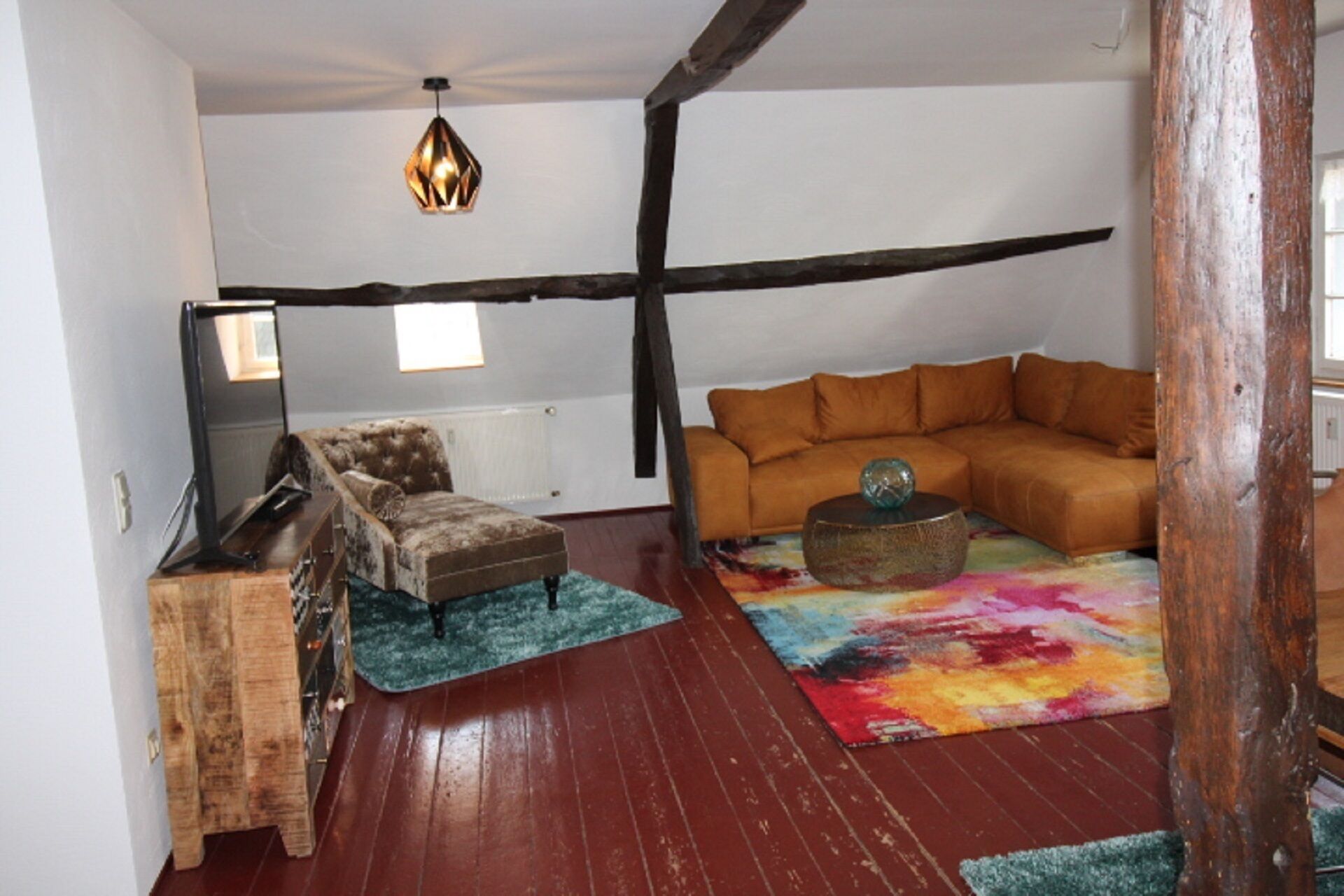Un salon chaleureux avec un canapé marron, un fauteuil à capitons, une table d’appoint en bois et un tapis coloré.