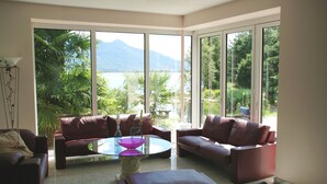Amplia sala de estar con ventanas grandes, una mesa de centro de vidrio y dos sofás de cuero.