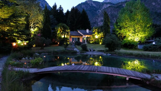 Una casa con un estanque, un puente de madera y montañas al fondo.