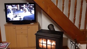 Olohuoneessa on televisio, joka on sijoitettu puiseen kaappiin, musta puukamina ja puinen portaikko.