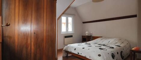 Ein Schlafzimmer mit einem Holzschrank, einem Bett mit Punkte-Bettbezug, einem Nachttisch und einem Fenster mit Jalousien.