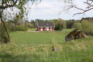 Una casa roja con puerta y ventanas blancas, rodeada por un campo cubierto de hierba y árboles.