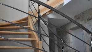 A spiral staircase with wooden steps and metal railings, leading to a stone wall and a door.
