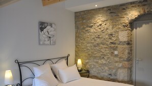 A bedroom with a stone wall, a bed with white bedding, two bedside lamps, and a door.
