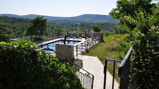 A pool area with a view of hills, surrounded by greenery and a stone structure.