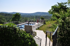 Un espace piscine offrant une vue sur les collines, entouré de verdure et agrémenté d’une structure en pierre.