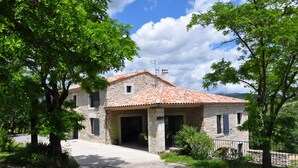 A stone house with a tiled roof, a covered patio, and a gravel driveway.