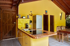 A kitchen with a yellow wall, wooden cabinets, a stainless steel sink, a white refrigerator, and a wooden dining table with chairs. - Kaz a Coco, Yellow Villa 2 bdrms, private pool (Deshaies)