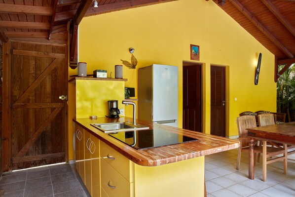 A kitchen with a yellow wall, wooden cabinets, a stainless steel sink, a white refrigerator, and a wooden dining table with chairs.