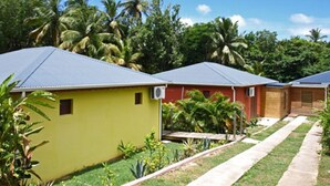 A row of single-story buildings with a flat roof, surrounded by lush greenery and palm trees. - Kaz a Coco, Yellow Villa 2 bdrms, private pool (Deshaies)