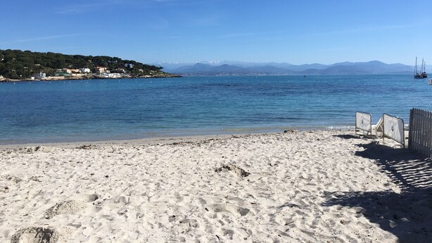 A beach with white sand, a clear blue sea, and a distant mountain range.