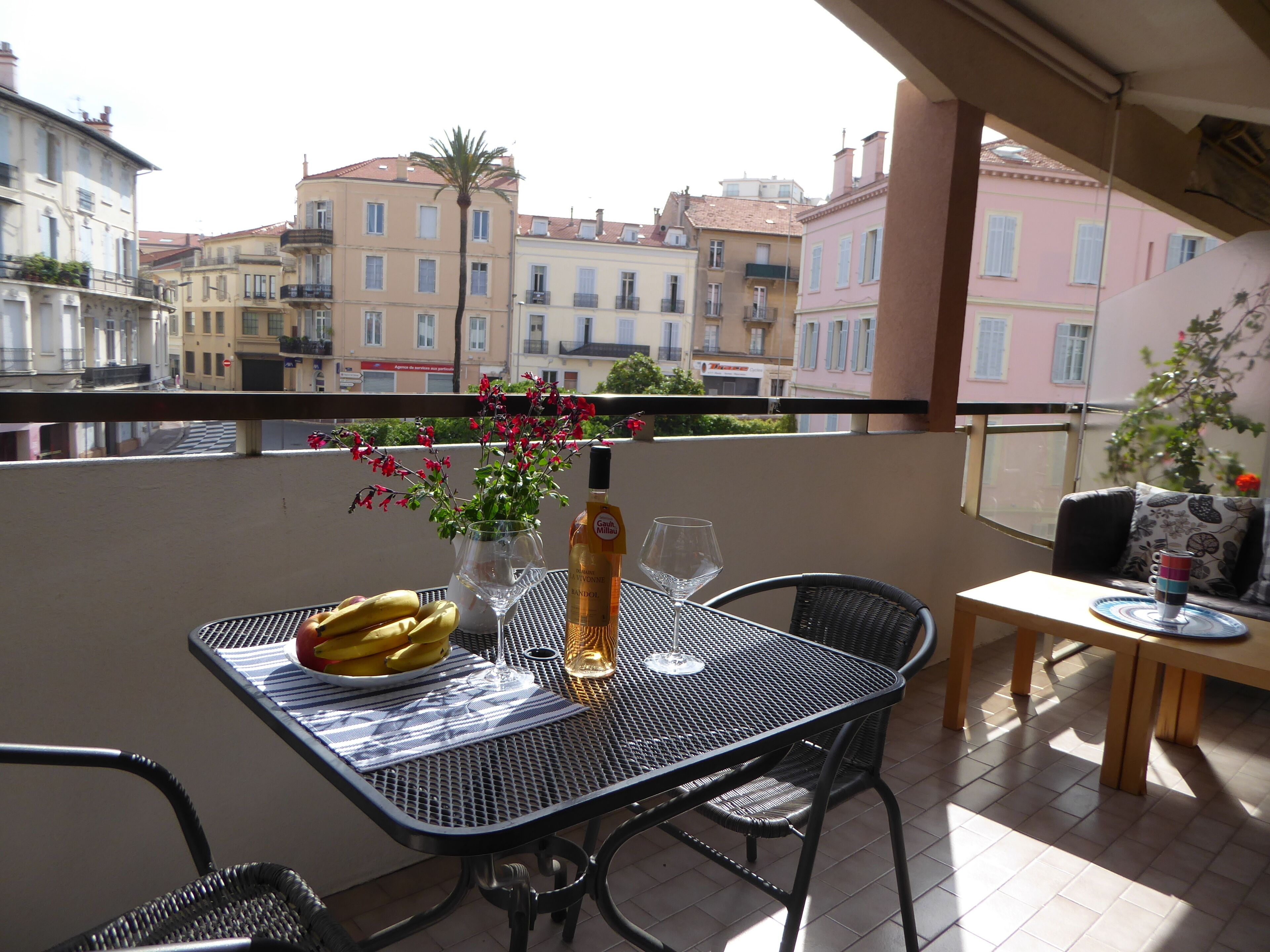 A balcony with a table set for two, featuring a bottle, glass, and fruit.